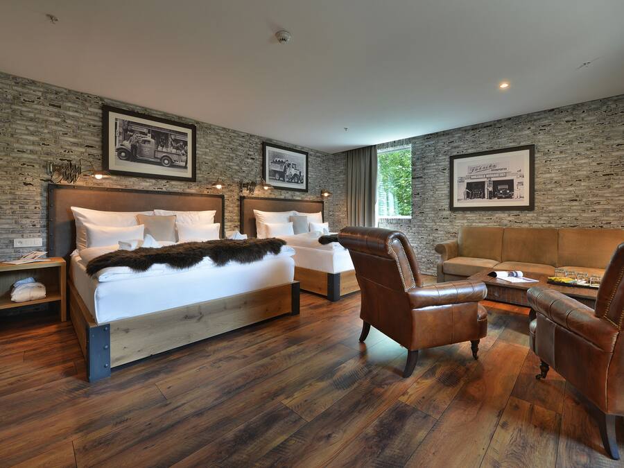 A modern bedroom with a large bed, two side tables, a leather armchair, a wooden coffee table, and a sofa.