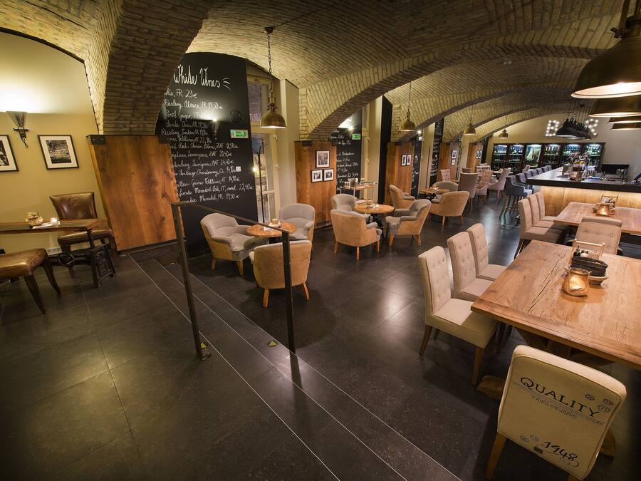 Een restaurant met een bakstenen plafond, houten tafels en stoelen. Er is een krijtbordmenu aan de muur en een bar in de achtergrond.