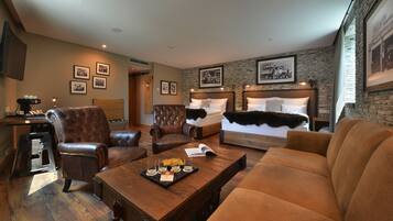 Une chambre d’hôtel avec un grand lit, deux fauteuils en cuir, une table basse en bois avec des verres et un plateau, et des tableaux encadrés aux murs.