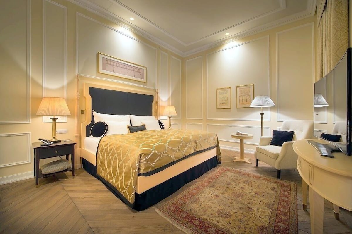 A hotel room with a large bed, bedside tables, a desk, a chair, and a mirror.