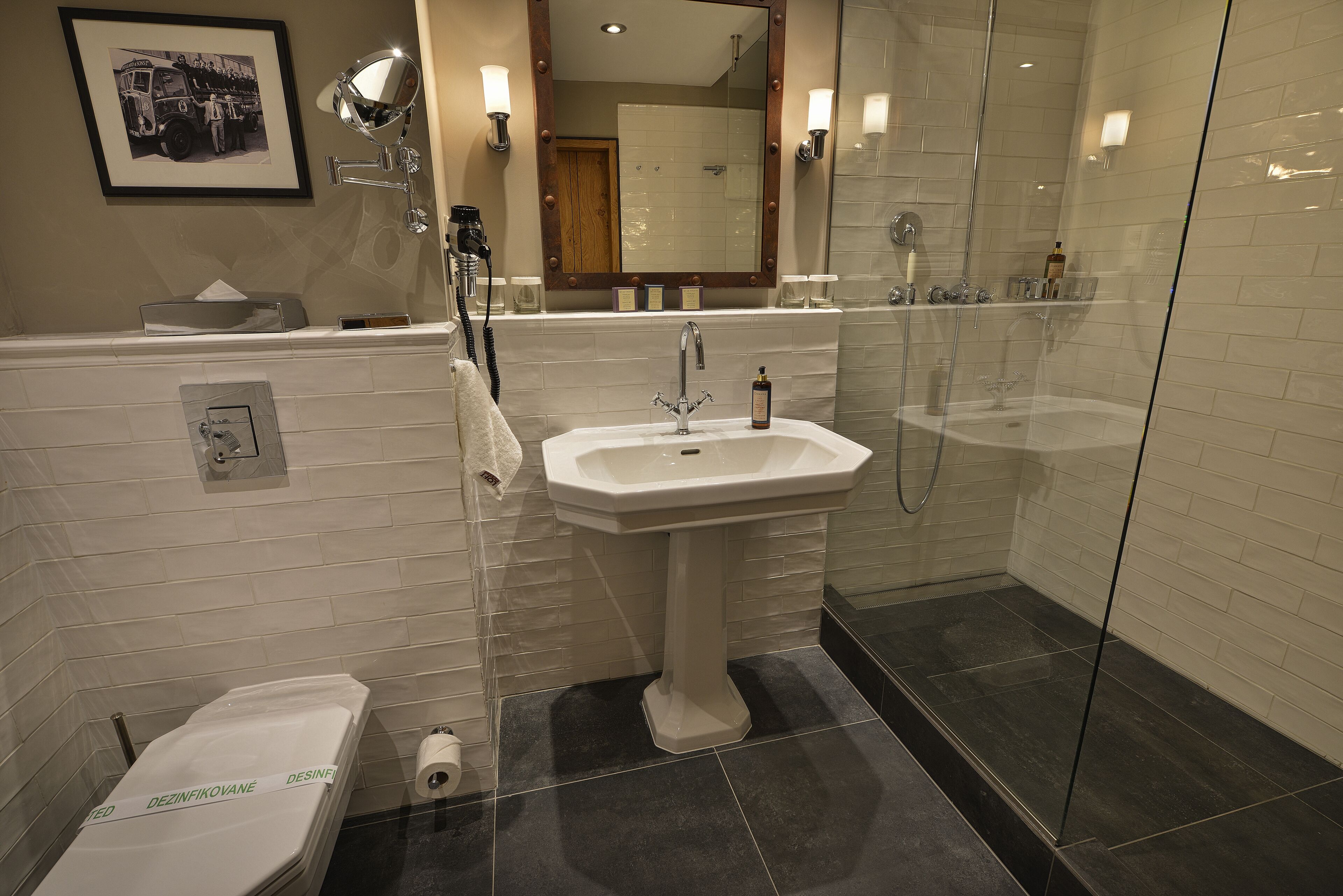 A modern bathroom with a white sink, a glass shower enclosure, and a framed picture on the wall.