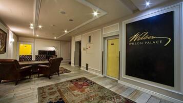 En rymlig hotellobby med en stor, svart skylt med texten ”Wilson Palace”, en matplats med bruna läderstolar och en mönstrad matta på golvet.