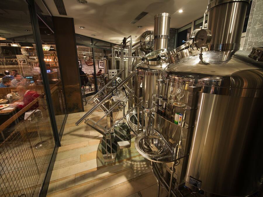 Een moderne bar met roestvrijstalen apparatuur, een trap naar een lager gelegen niveau en een zithoek met tafels en stoelen.
