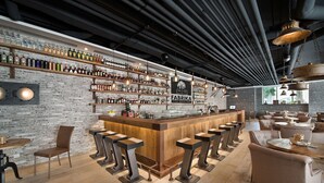 Zona de bar con pared de ladrillo, mostrador de madera y varios taburetes.