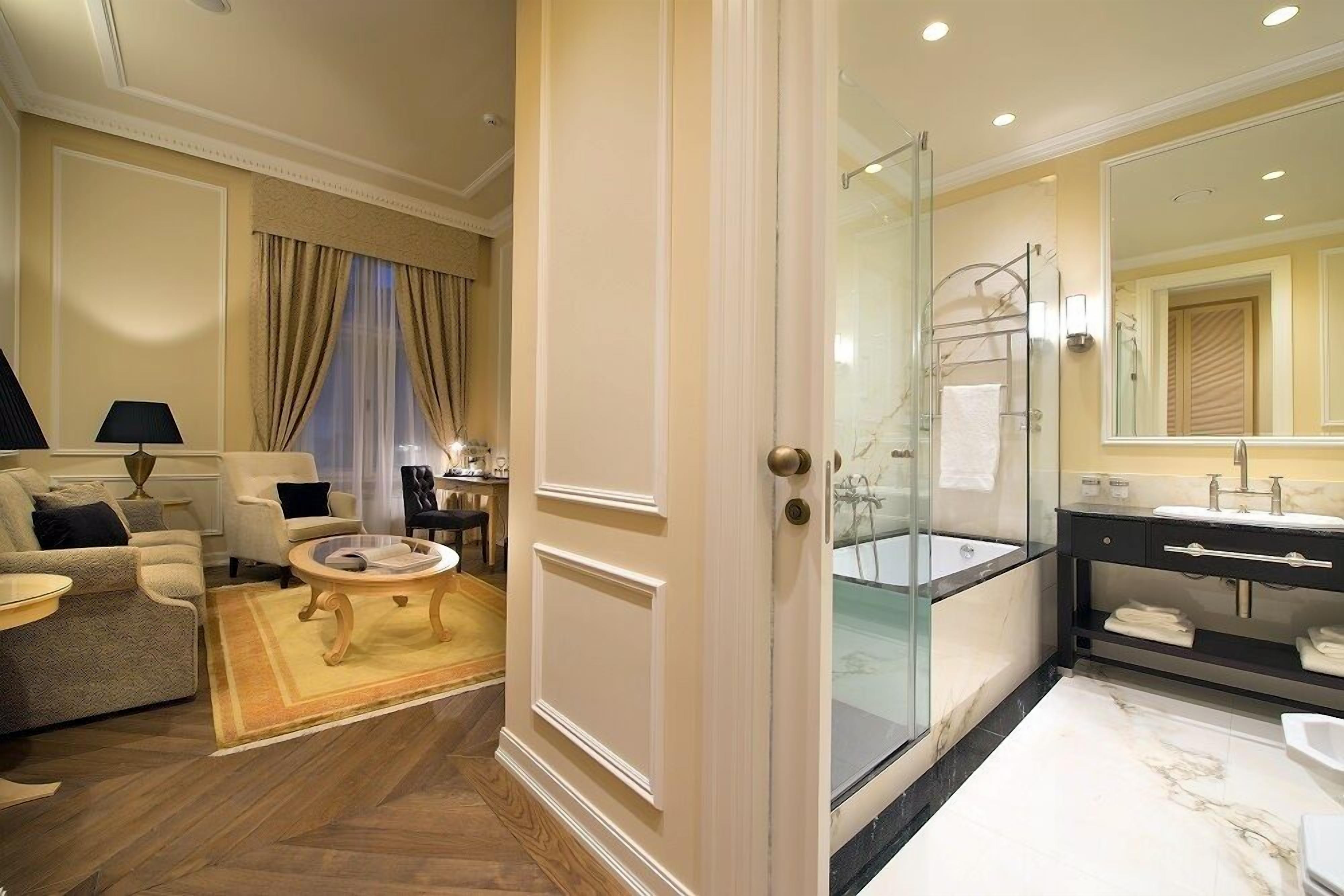 A spacious living room with a sofa, armchair, and coffee table, adjacent to a bathroom with a glass-enclosed shower and a vanity with a mirror.