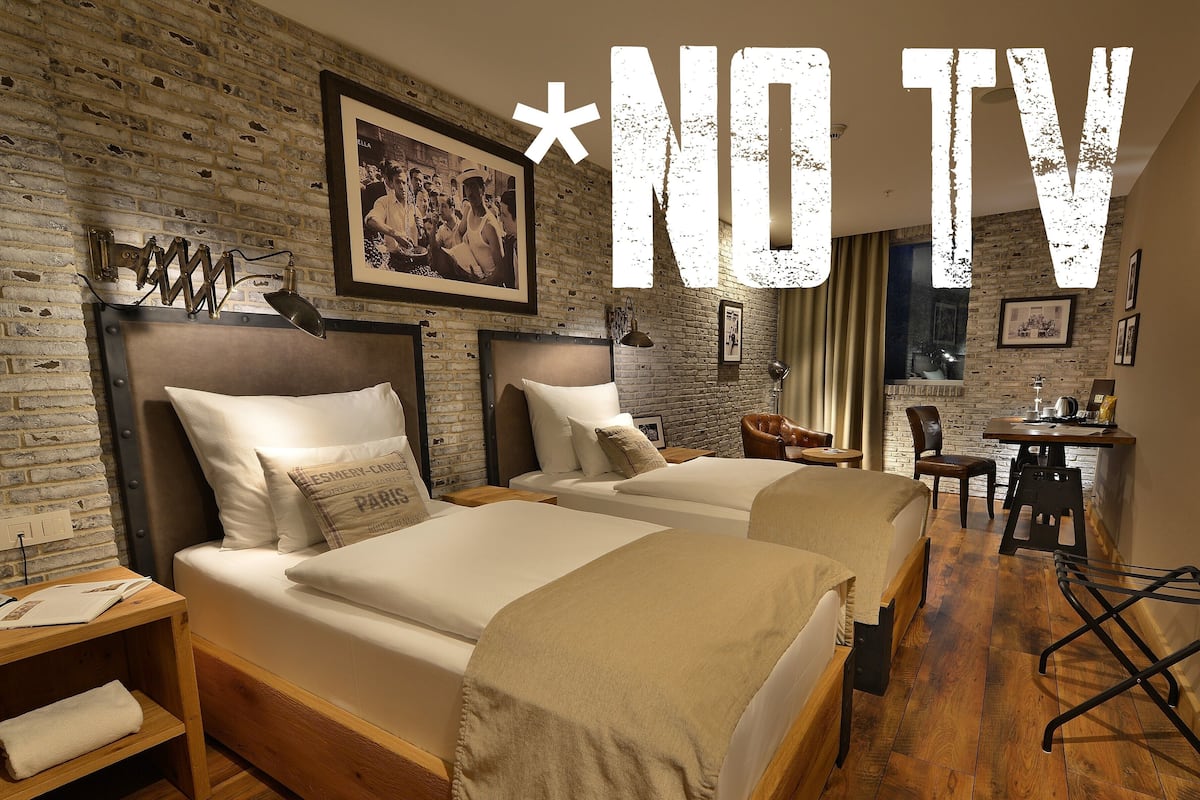 A hotel room with two beds, a brick wall, a dining area, and a TV sign.