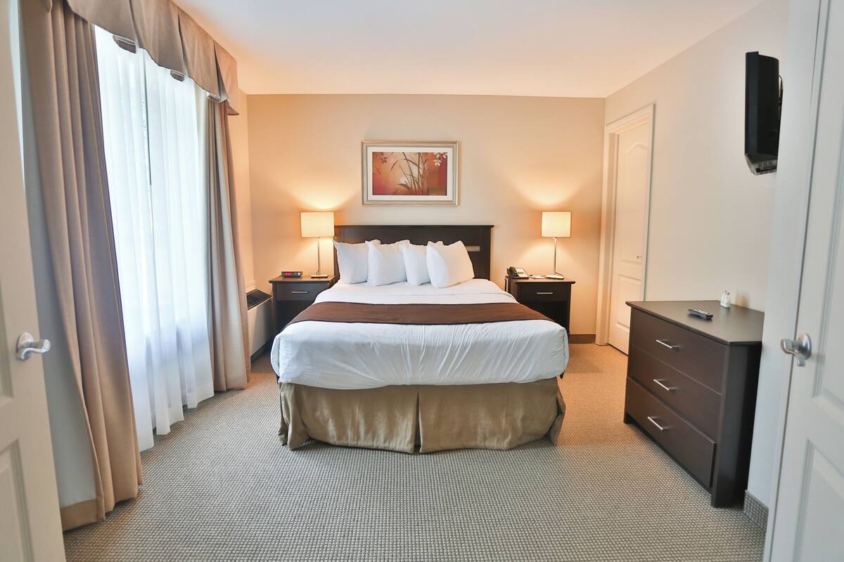 Un cuarto de hotel con una cama grande, dos mesitas de noche con lámparas, un aparador y un cuadro en la pared.