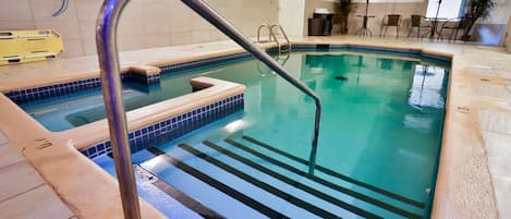 An indoor swimming pool with a metal ladder, tiled steps, and a clear blue water surface.