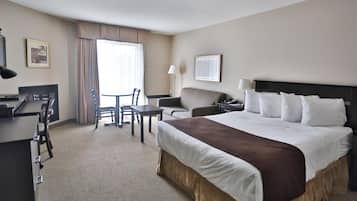 Habitación de hotel con una cama grande, un escritorio, una silla, un sofá y una ventana con cortinas.