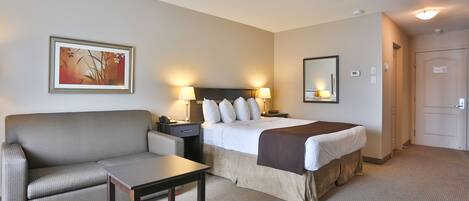A hotel room with a bed, a sofa, a bedside table, a lamp, and a painting on the wall.