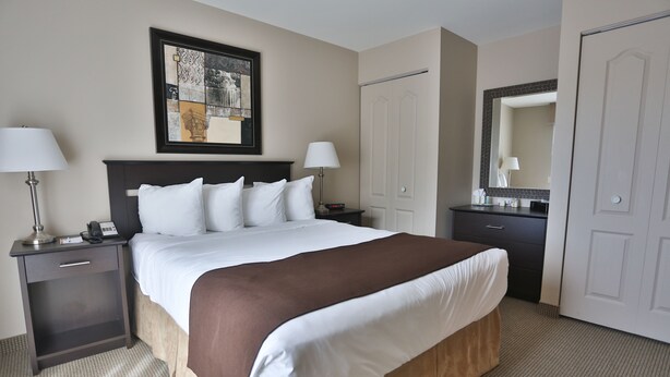 Habitación de hotel con una cama grande, dos mesitas de noche, un tocador, un aparador, un espejo y una obra de arte enmarcada en la pared.