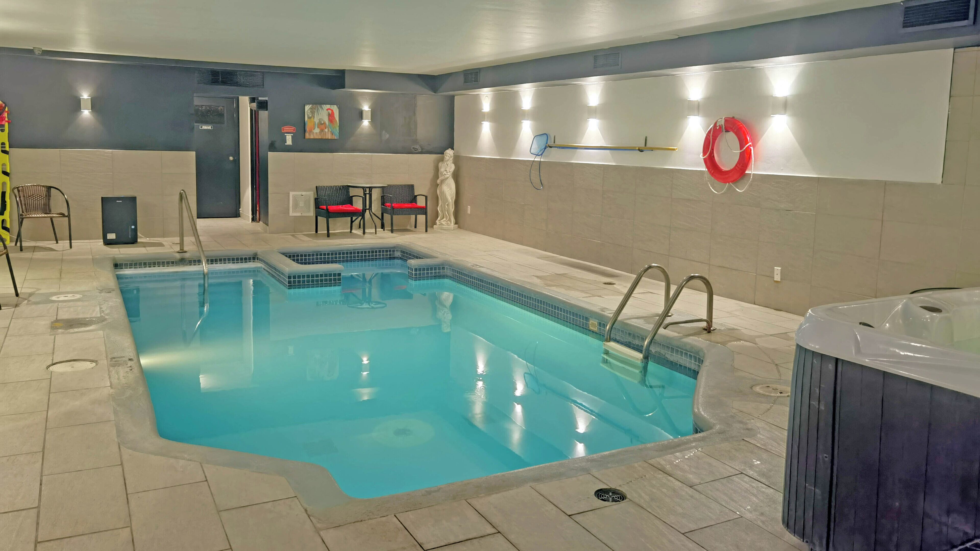 Una piscina interior con un jacuzzi, suelo de baldosas y una zona de estar con sillas.