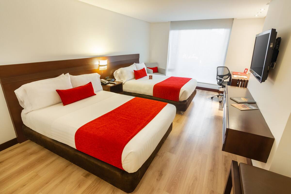 Habitación de hotel con dos camas, un escritorio, una silla, un televisor y una ventana.