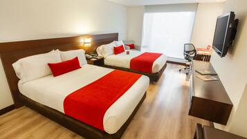 A hotel room with two beds, a desk, a chair, a TV, and a window.