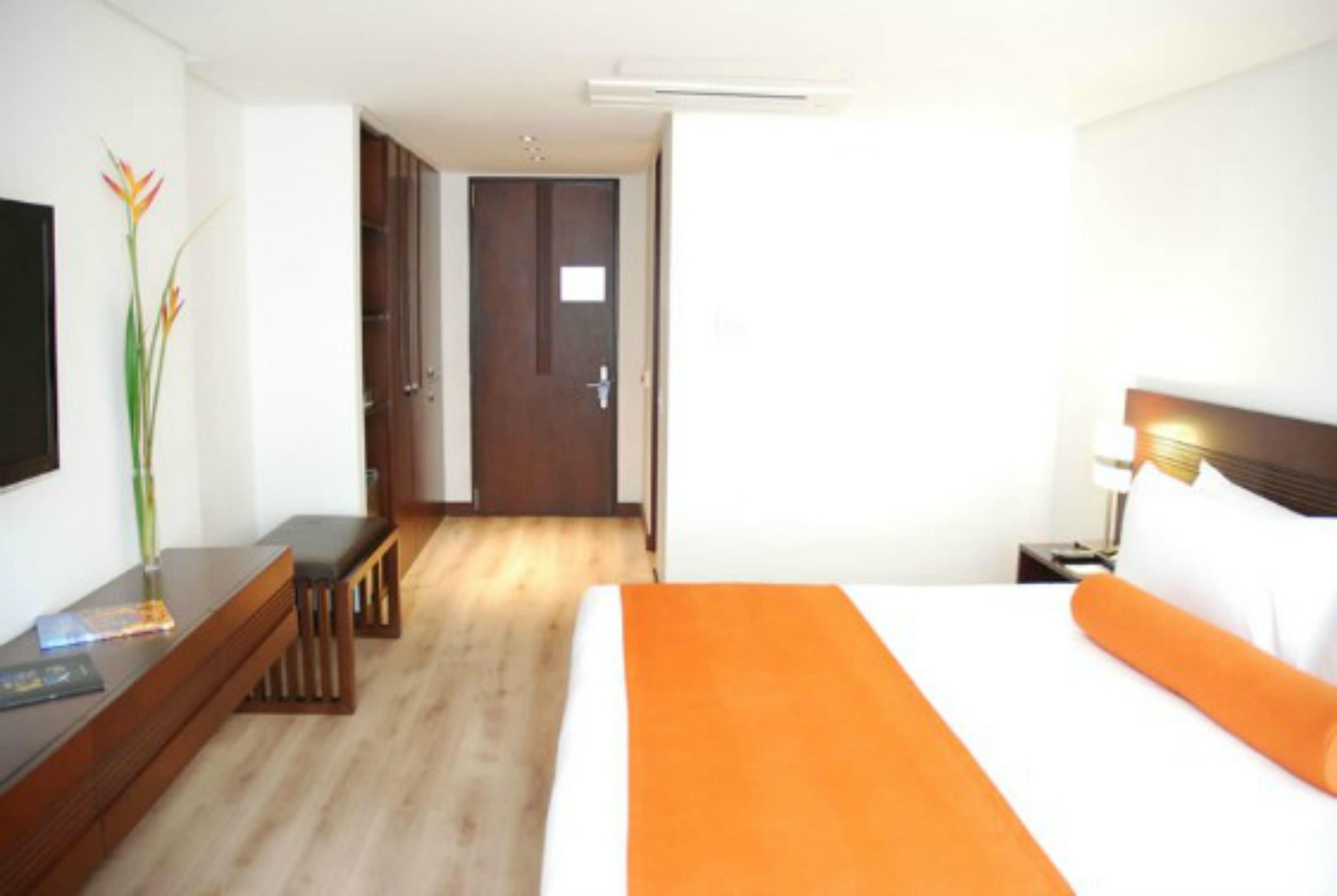 Una camera d'albergo con un letto, una scrivania, una sedia, un comodino e una porta.