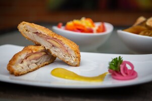 Un plato con un sándwich cortado por la mitad, un pepinillo y un tazón pequeño de ensalada.