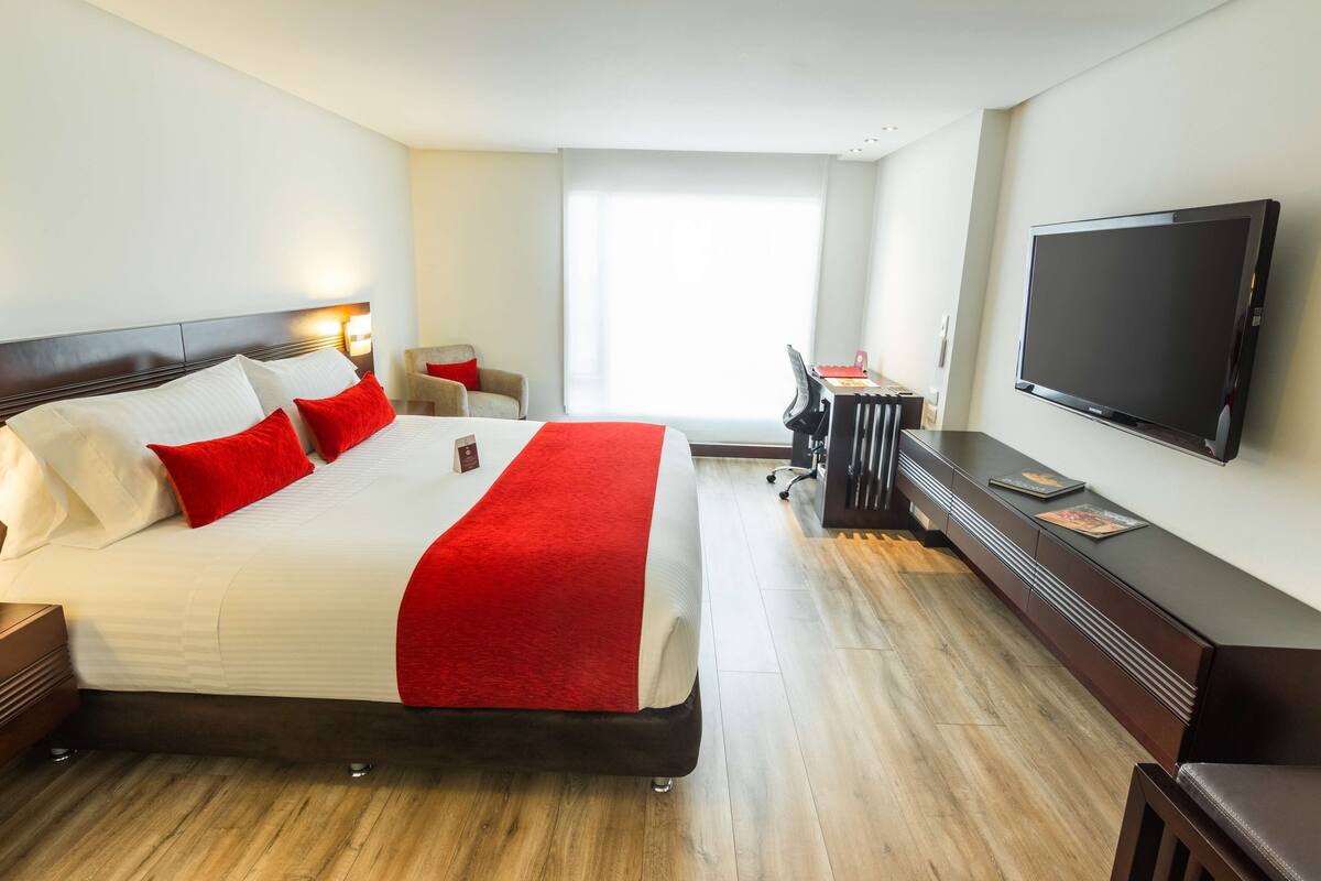 Habitación de hotel con una cama grande, un escritorio, una silla, un televisor y una ventana.