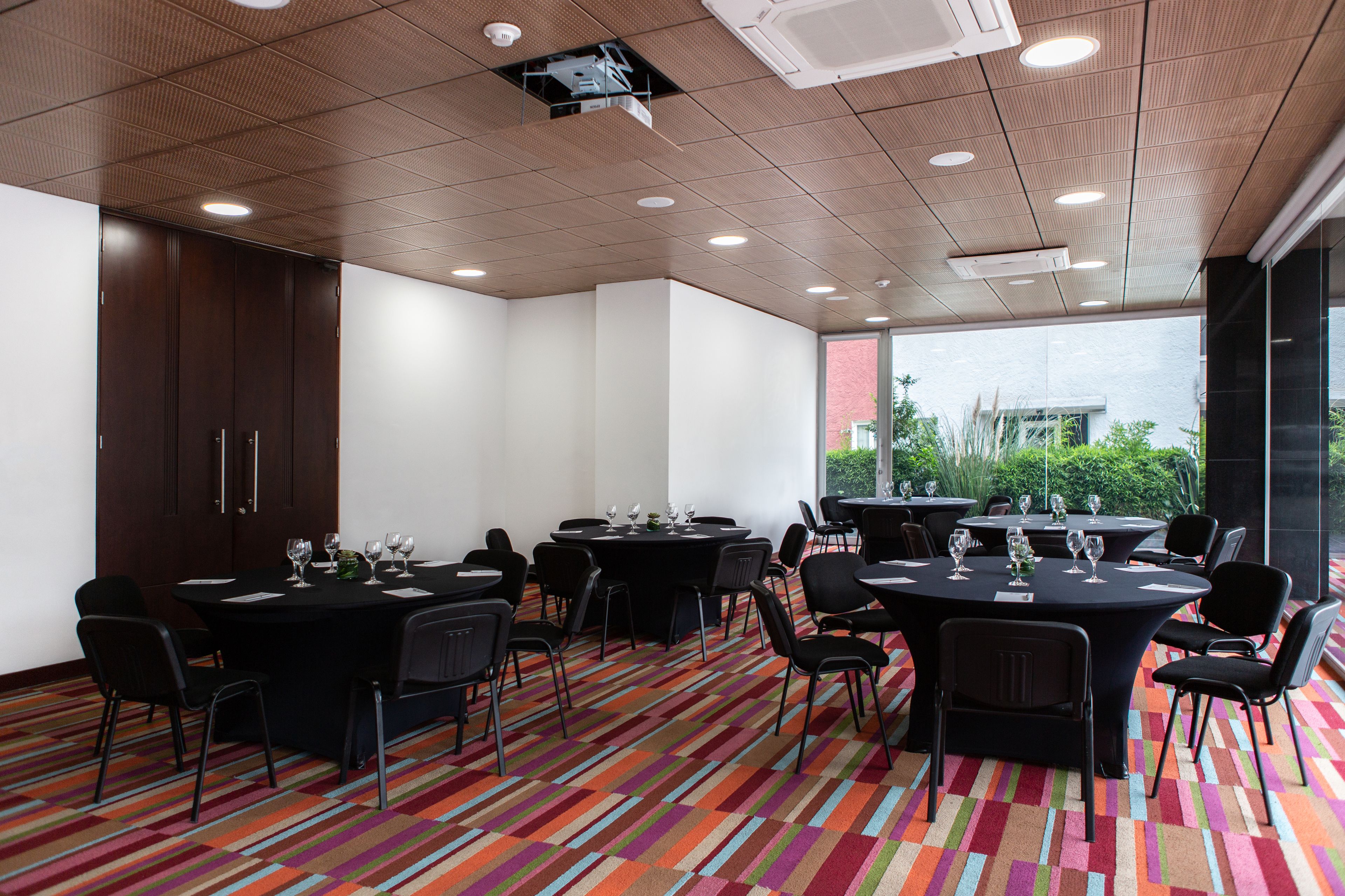 A conference room with multiple tables, black chairs, and a colorful striped carpet.