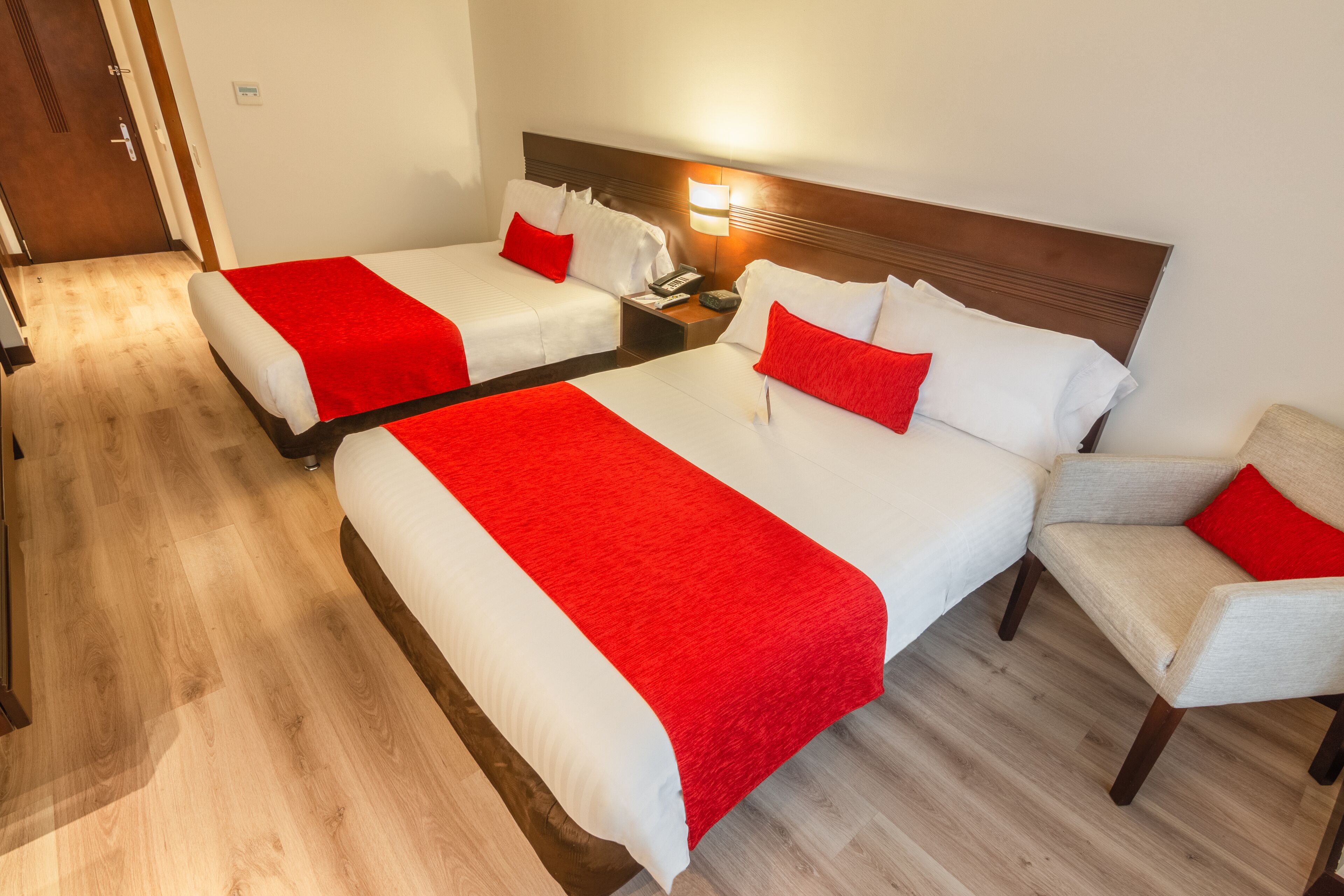 A hotel room with two beds, a nightstand with a phone, a chair, and a wooden floor.