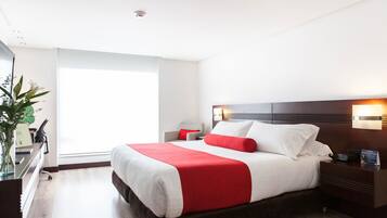 A modern hotel room with a large bed, a bedside table, a nightstand, a desk with a chair, and a window.
