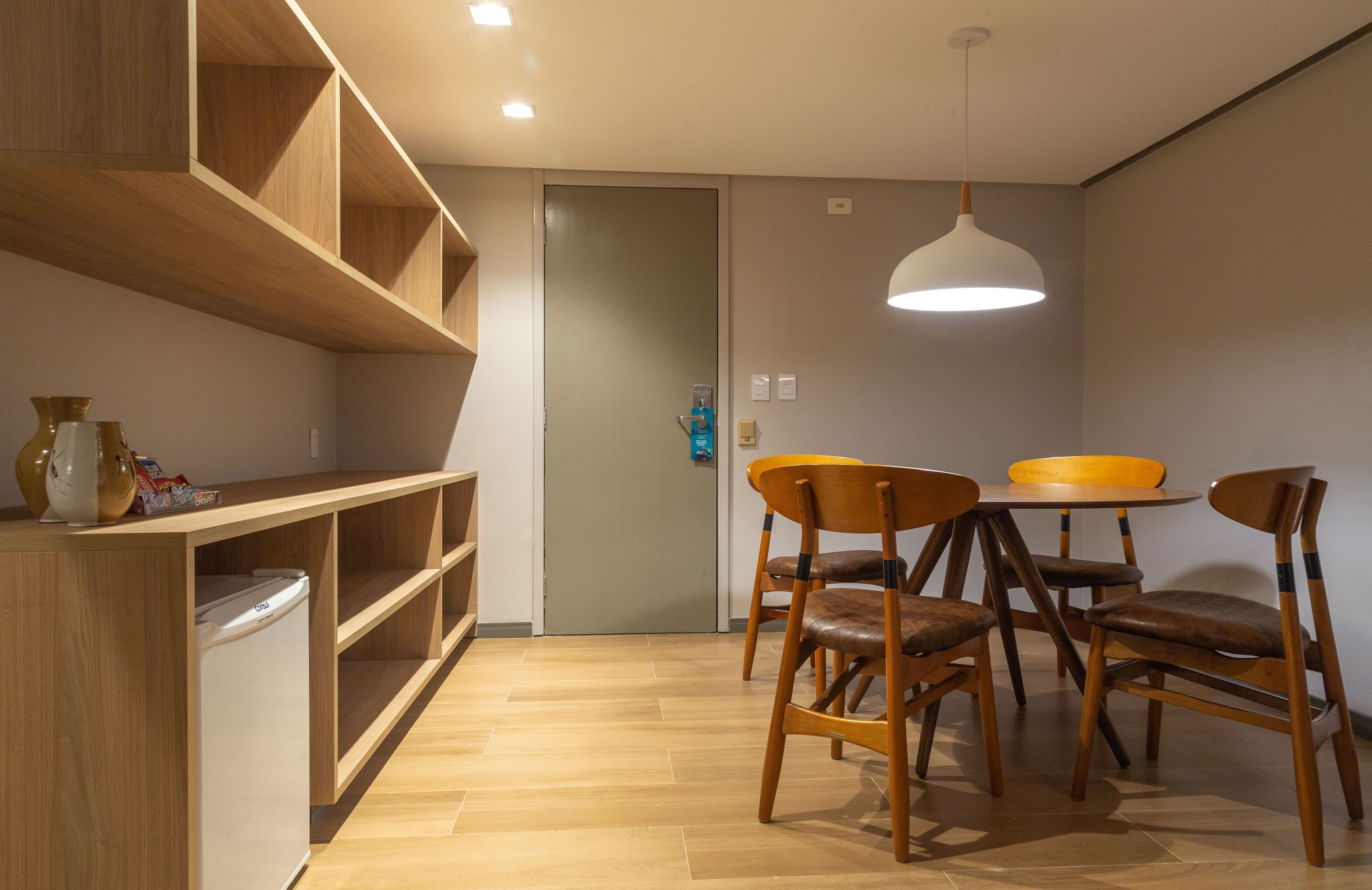 Une cuisine compacte avec des meubles en bois, un réfrigérateur encastré, une table à manger avec quatre chaises et un luminaire suspendu.