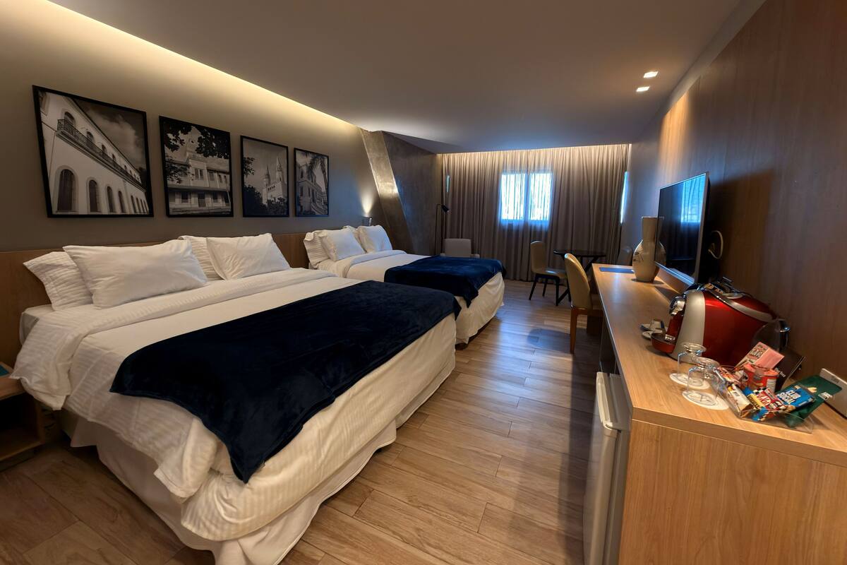 A hotel room with two beds, a desk with a TV, and a minibar.