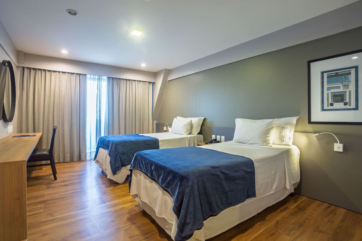 A hotel room with two beds, a desk, and a chair.