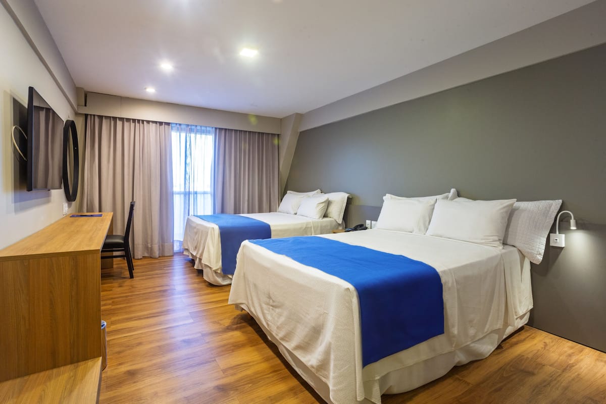 A hotel room with two beds, a desk, and a TV mounted on the wall.
