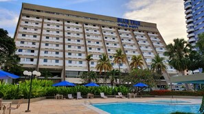 Un hotel con zona de piscina, sillas de descanso y palmeras.