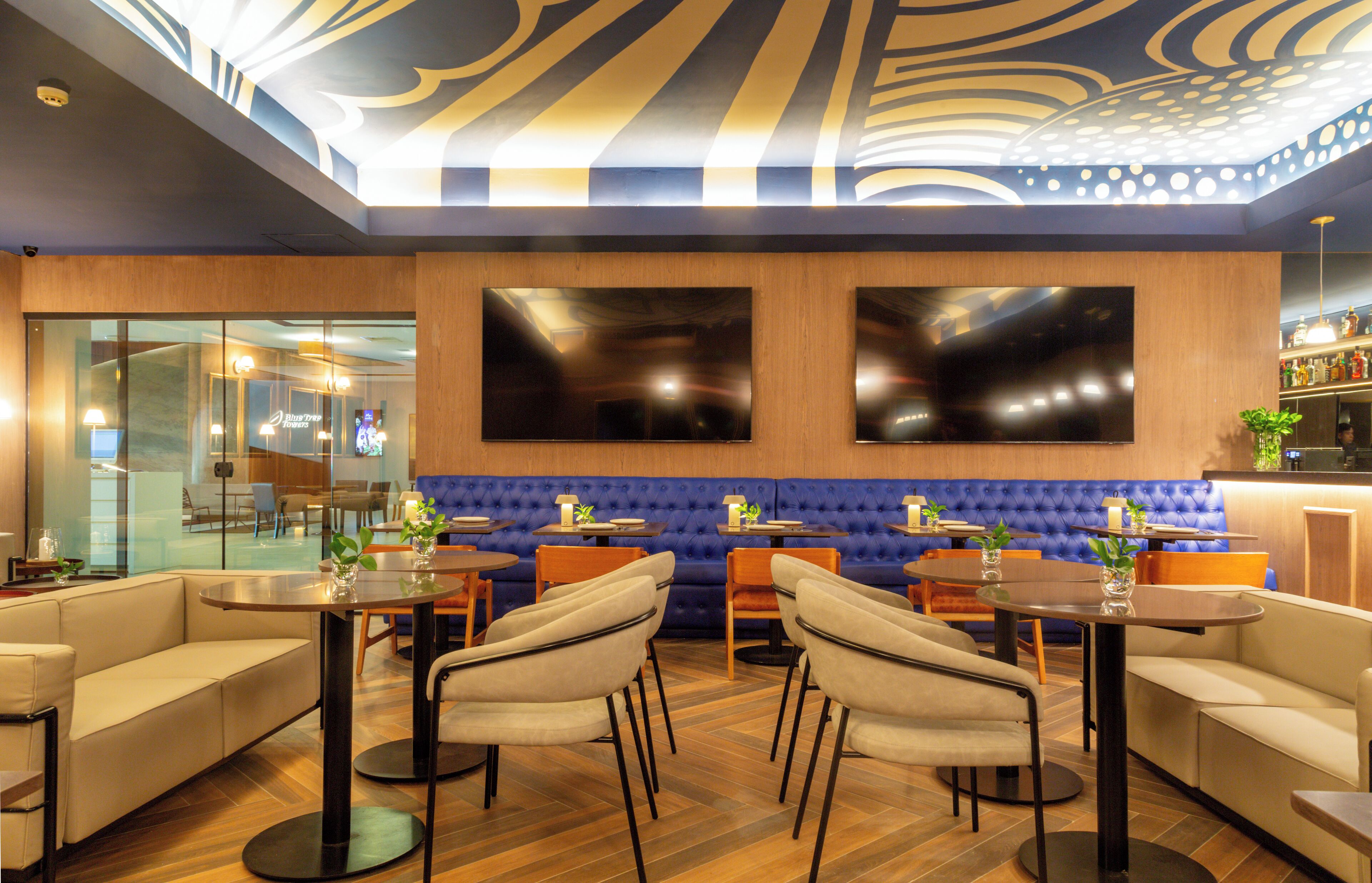 A modern interior with a blue cushioned seating area, wooden tables, and a bar area with a variety of bottles.