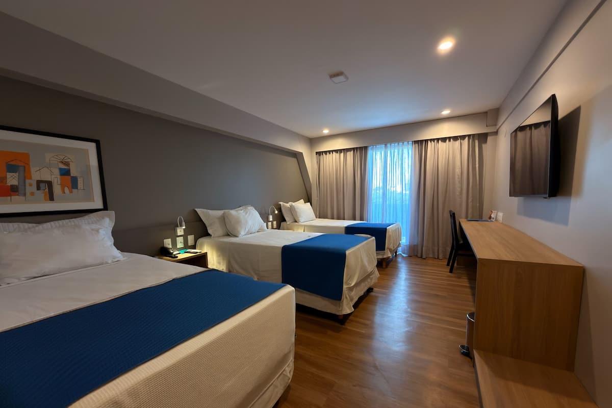 A hotel room with two beds, a desk, a chair, and a TV on the wall.