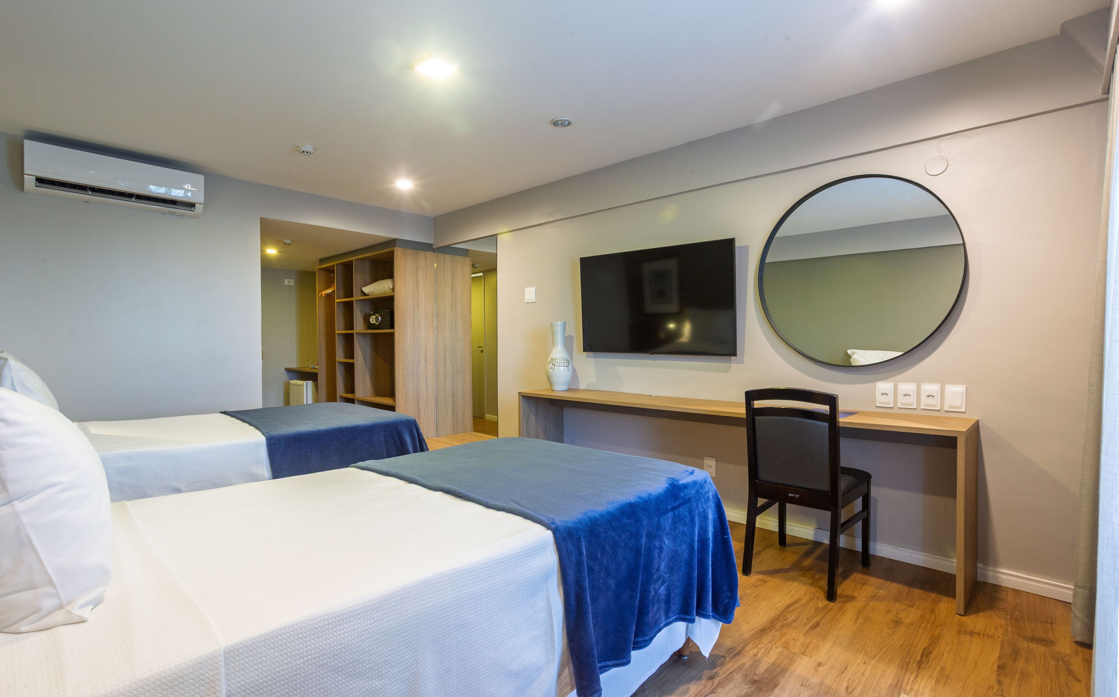 Une chambre d’hôtel avec deux lits, un bureau, une chaise, une télévision et un miroir.