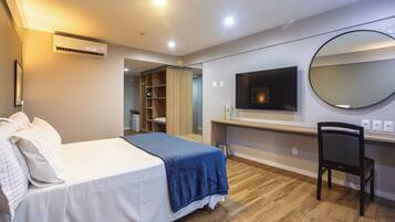 Una camera d'albergo con un letto, una scrivania, una sedia, una televisione, uno specchio e un condizionatore d'aria.