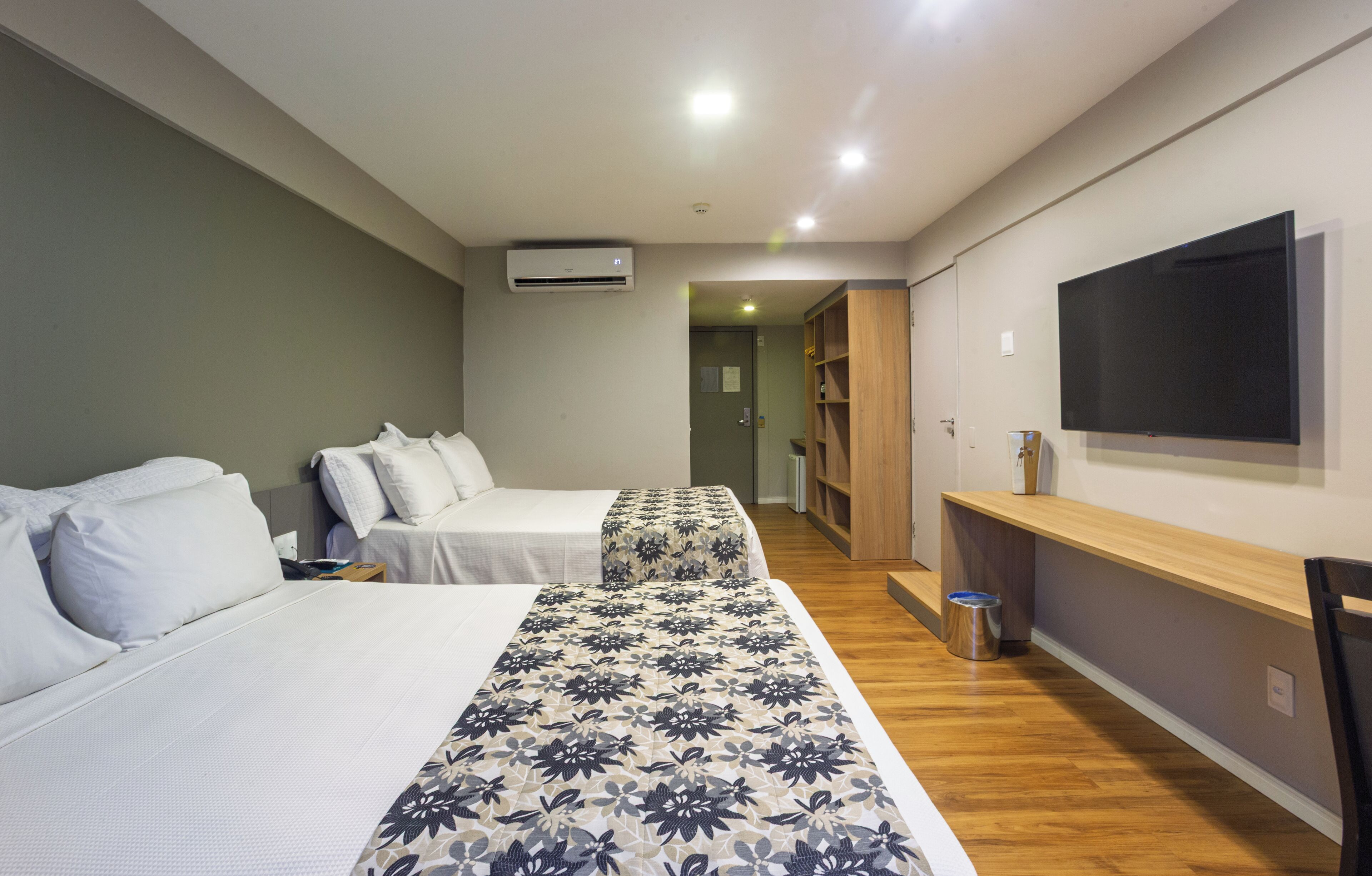 Une chambre d’hôtel avec deux lits, une télévision, une étagère en bois et une poubelle.