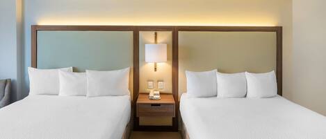 A hotel room with two beds, a nightstand with a lamp, and a phone.