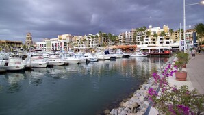 A marina with multiple boats docked, a waterfront promenade with potted plants, and a variety of buildings in the background. - Fairfield by Marriott Los Cabos (Cabo San Lucas)