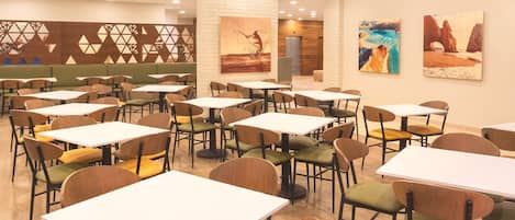A restaurant with multiple tables and chairs, wooden flooring, and wall art.