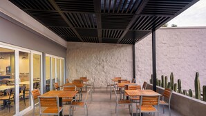 An outdoor dining area with wooden tables and metal chairs, a stone wall, and a cactus garden. - Fairfield by Marriott Los Cabos (Cabo San Lucas)