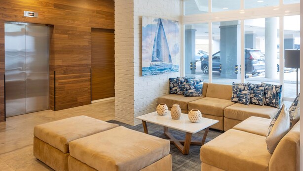 A modern lobby with a wooden wall, a white brick wall with a sailboat painting, beige sofas, and a table with decorative vases. - Fairfield by Marriott Los Cabos (Cabo San Lucas)