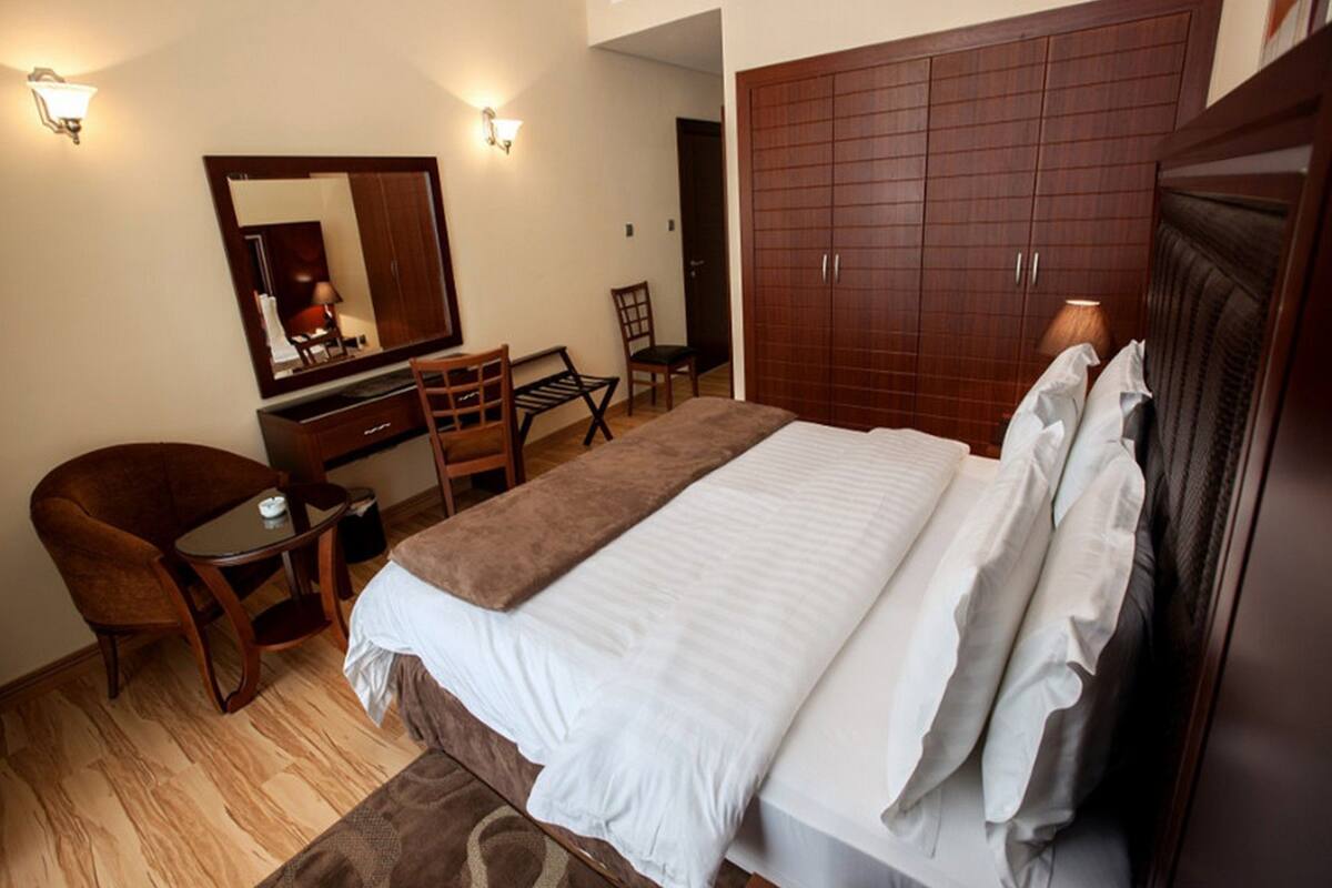 A bedroom with a bed, a desk, a chair, a wardrobe, and two wall-mounted lights.