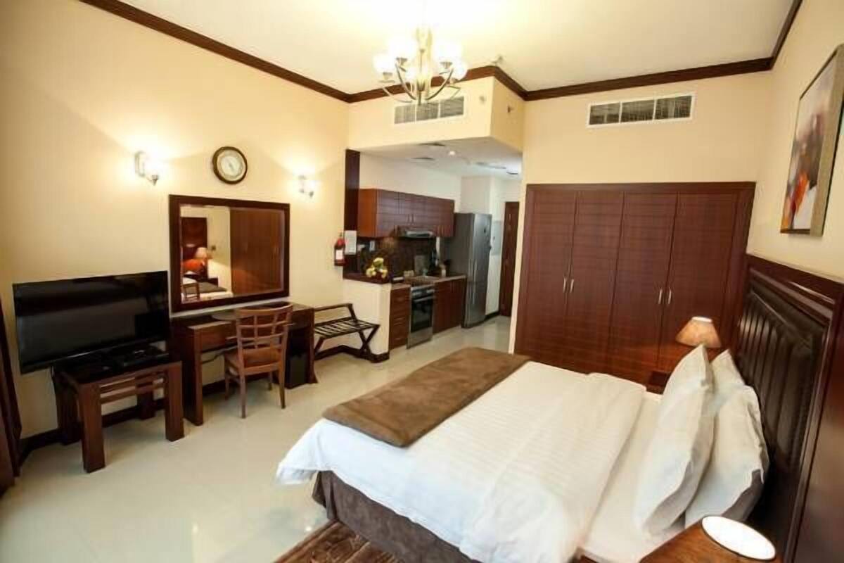 A hotel room with a bed, a TV, a desk, and a kitchenette.