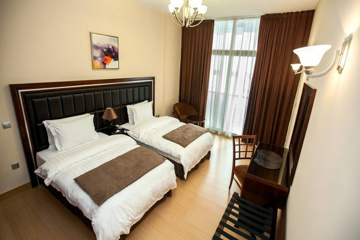 A hotel room with two beds, a desk, a chair, a lamp, and a painting on the wall.