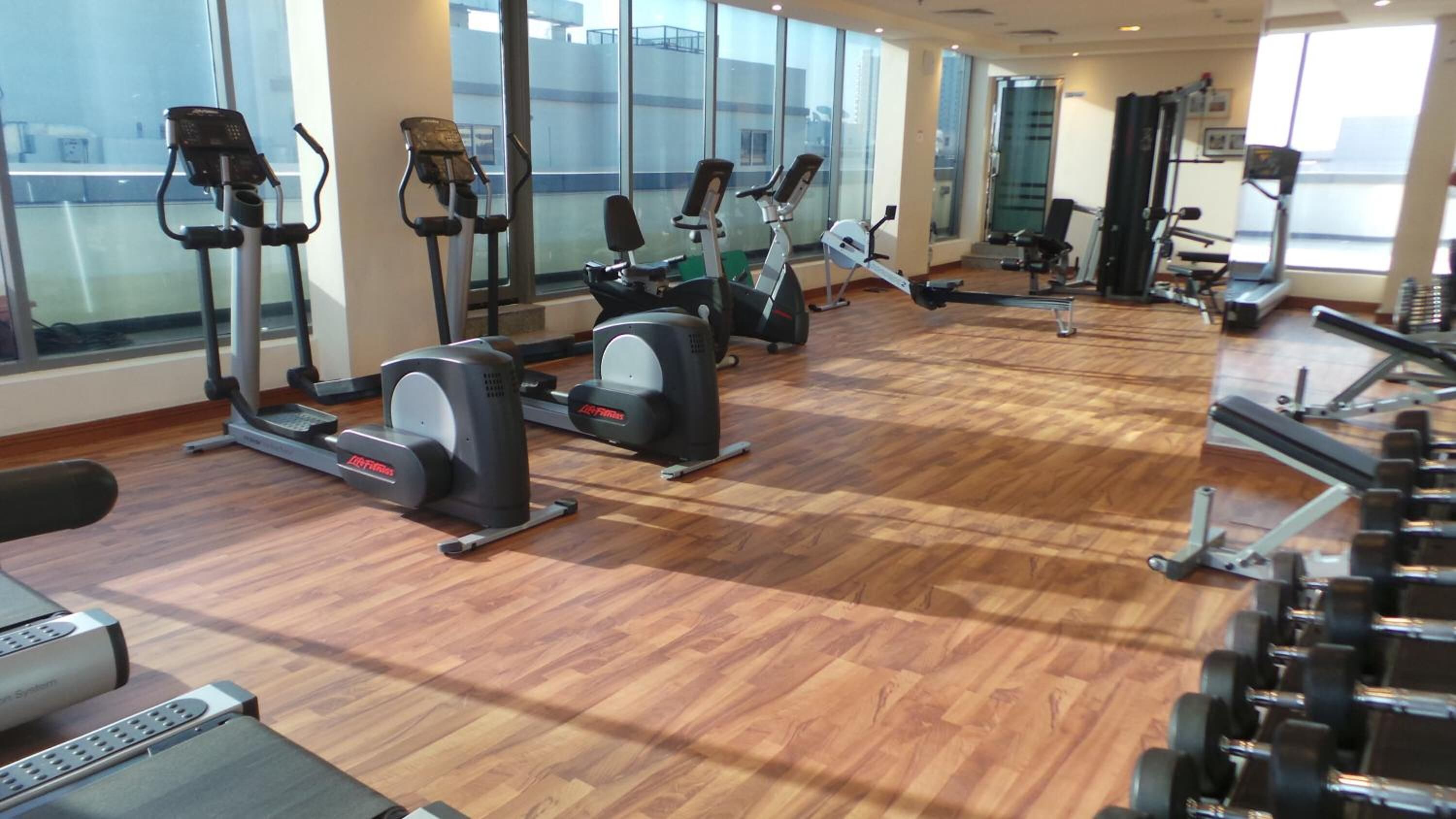 A gym with various cardio machines, weightlifting equipment, and large windows offering views of the city.