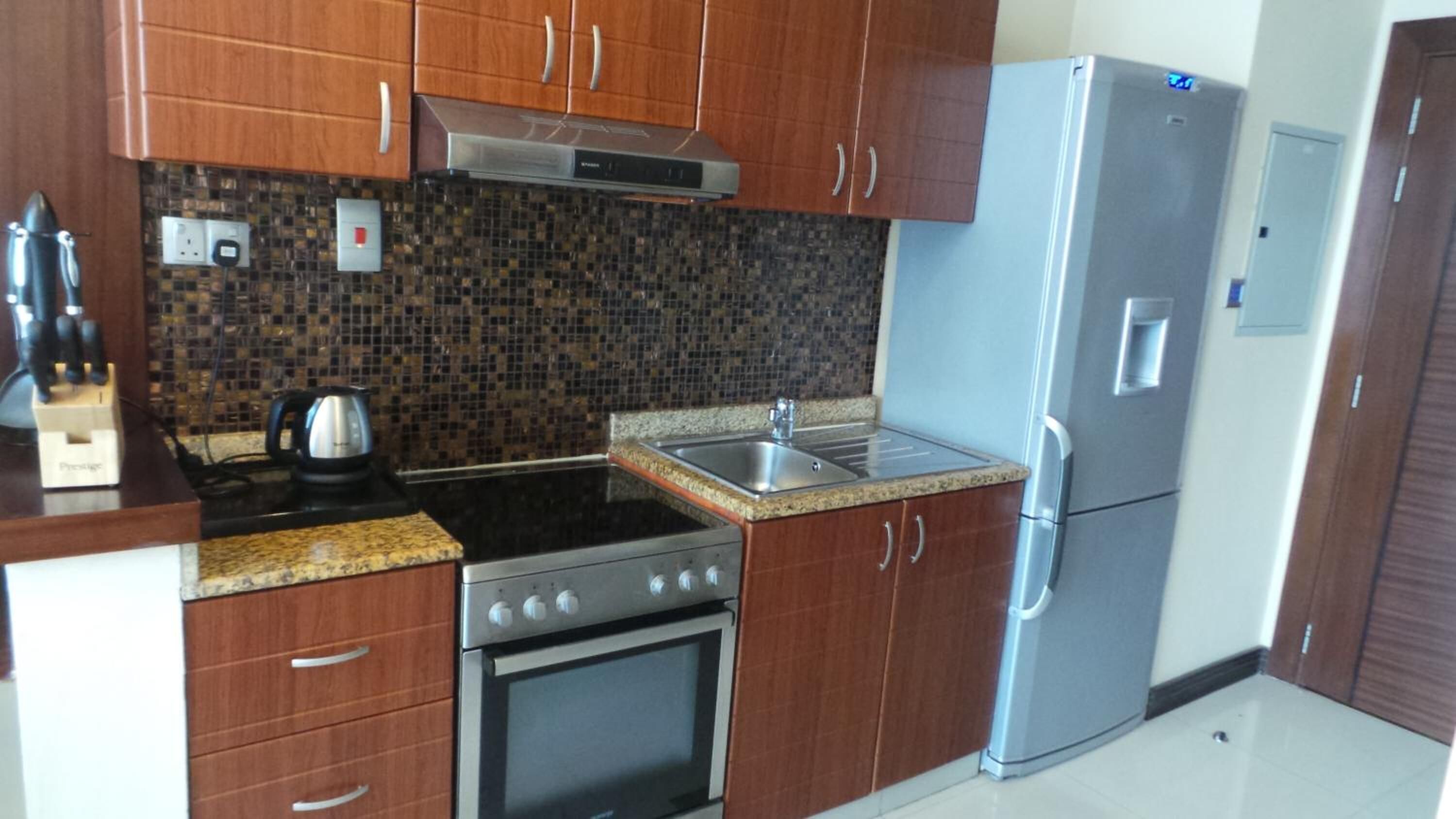 A kitchen with wooden cabinets, a granite countertop, a stainless steel stove, a sink, and a refrigerator.