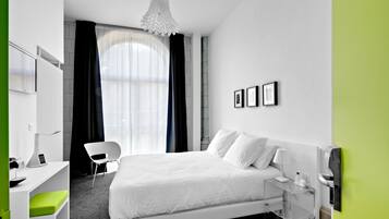 A modern hotel room with a large bed, a desk with a chair, a desk lamp, and a telephone.