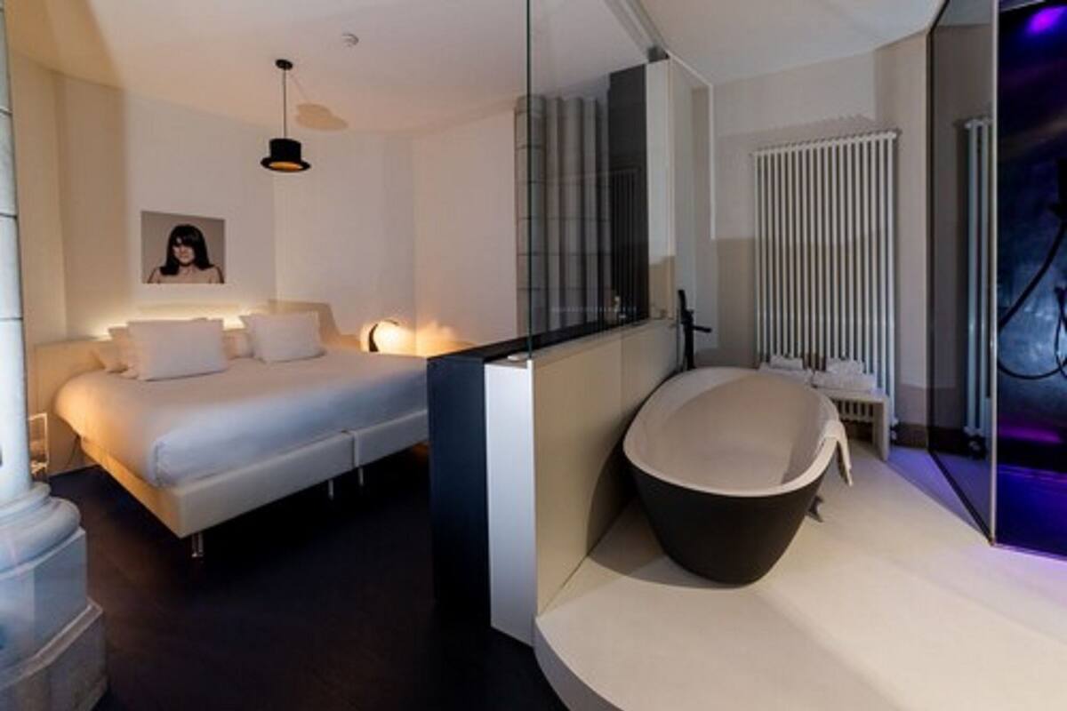 Un dormitorio moderno con una cama grande, una mesita de noche y un separador de vidrio que divide la habitación del baño.