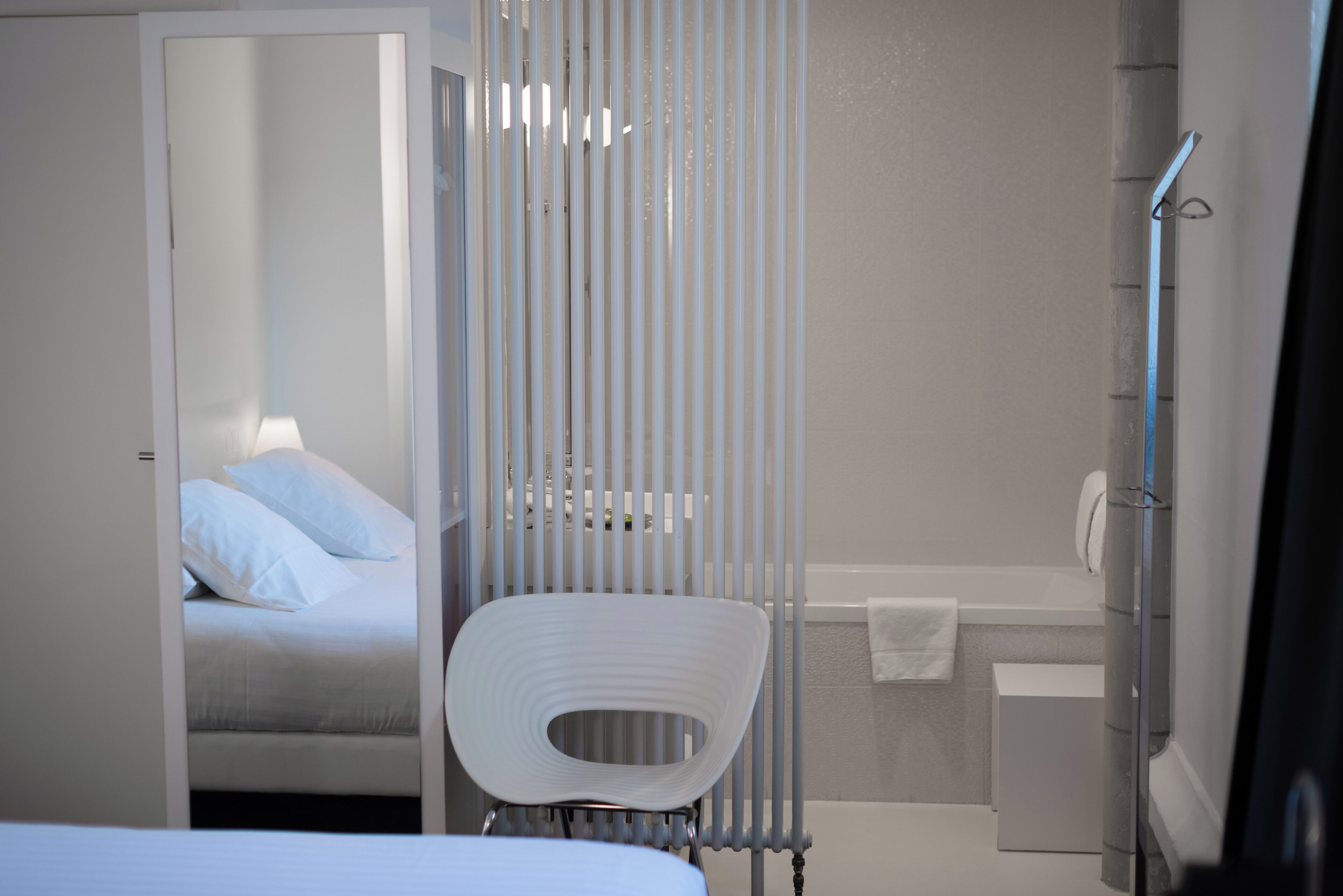 Een moderne badkamer met douche, toilet en wastafel. In de aangrenzende kamer staat een bed met wit beddengoed.