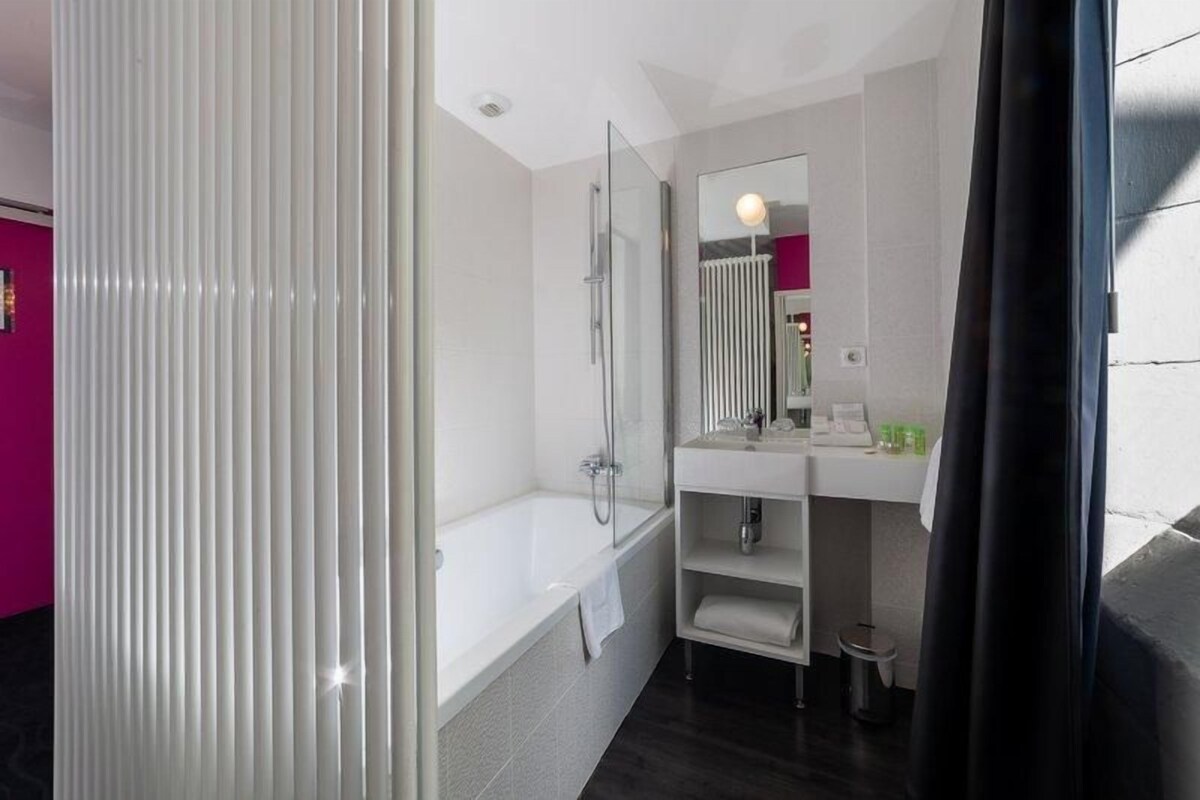 A modern bathroom with a bathtub, a glass shower enclosure, a white sink with a mirror, and a small trash bin.