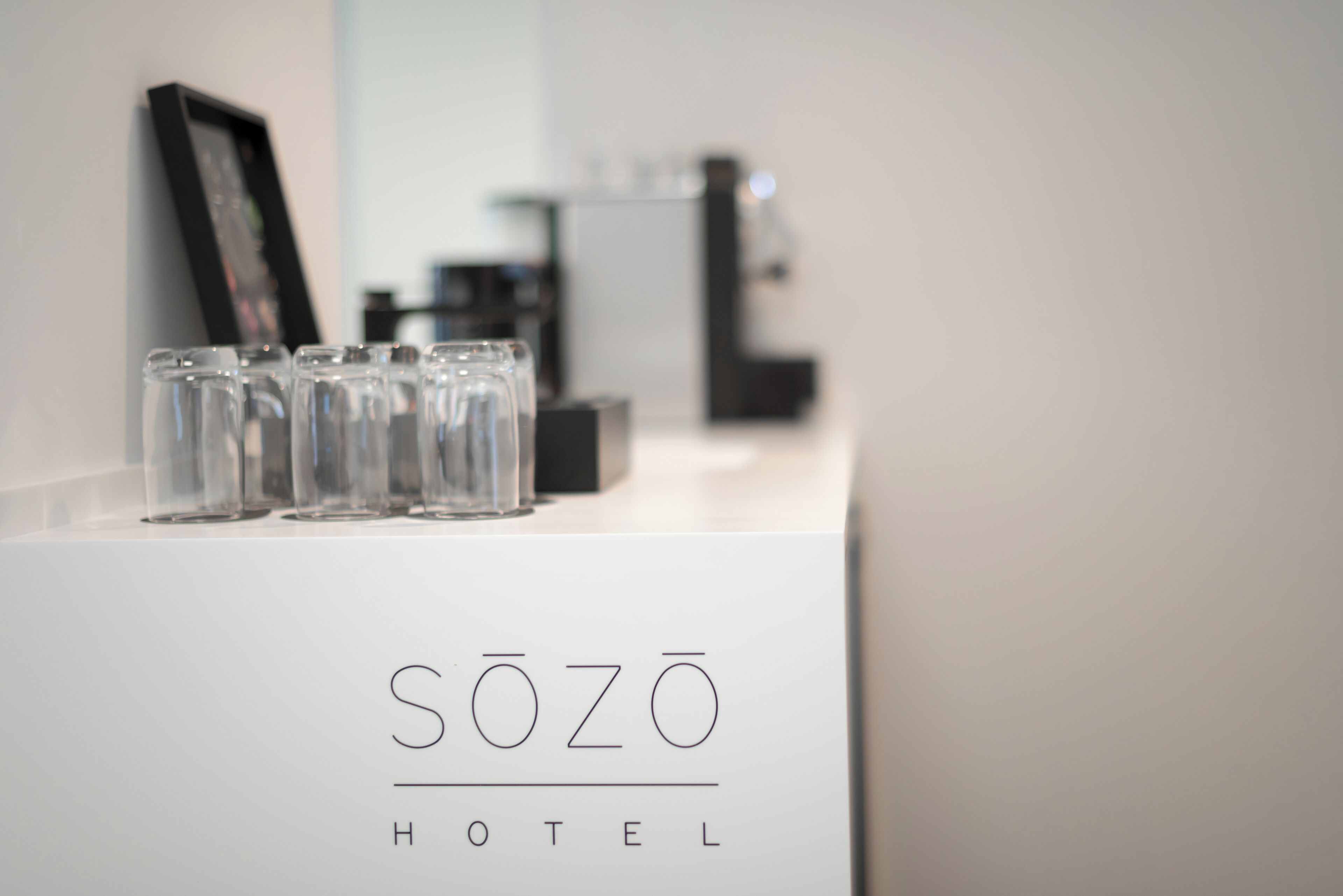 A hotel reception area with a sign reading "SÖZO HOTEL" and a row of glasses on a counter.