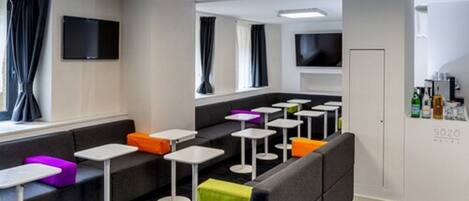 A modern hotel lobby with seating areas, tables, and a television screen.